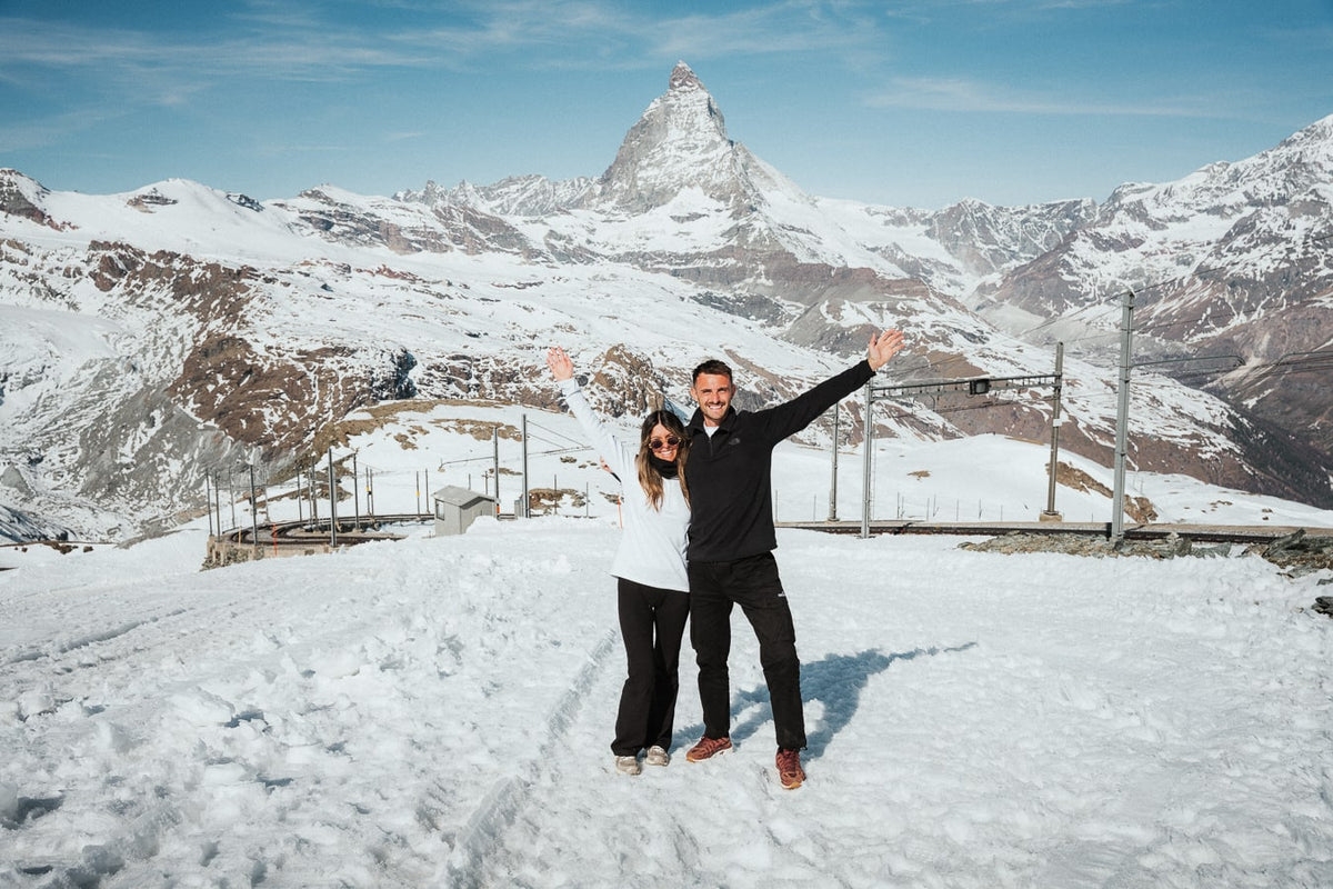 Lachie and Tarsh standing together in the snow with mountain peaks behind them.